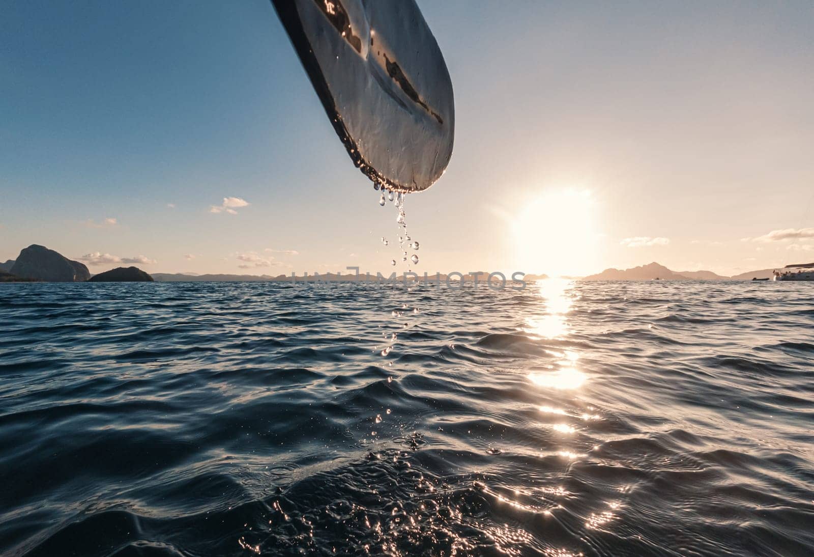 Kayak paddle dripping water at sunset in serene ocean landscape by Busker