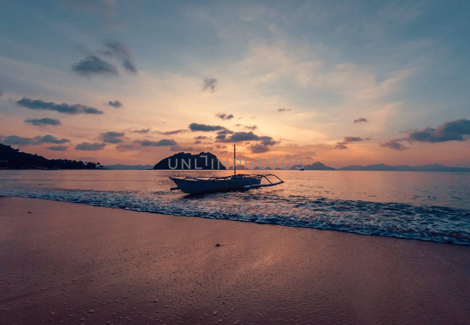 A small boat rests gently in the calm waters near a pristine beach as the sun sets.