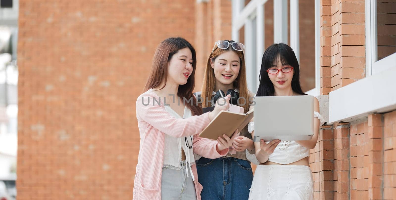 A group of female female students at an Asian university stood outside the classroom talking about their classes on laptops during break time. by wichayada