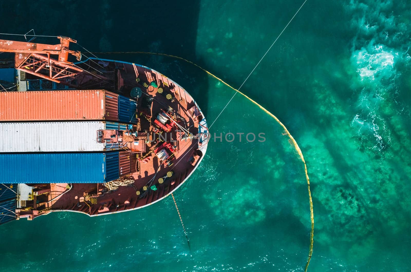 Aerial view of a container cargo ship stands aground after a storm with floating boom around the ship to prevent the spread of petroleum. Top down view of a ship bow