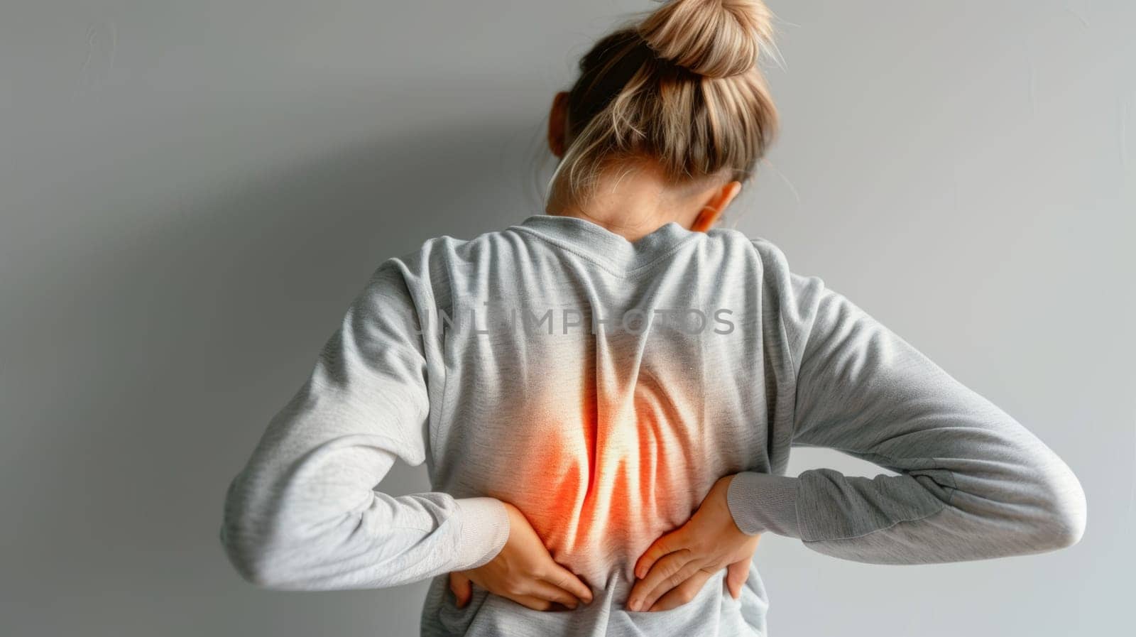 The image shows a woman from behind as she holds her lower back, a visual metaphor for sharp pain. The soft grey tones of her clothing contrast with the vibrant red depicted as pain