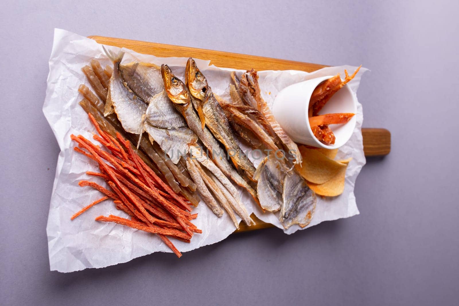 Assorted dried fish, fish skin, and fruit snacks on white paper on a wooden table, creating a vibrant culinary display.