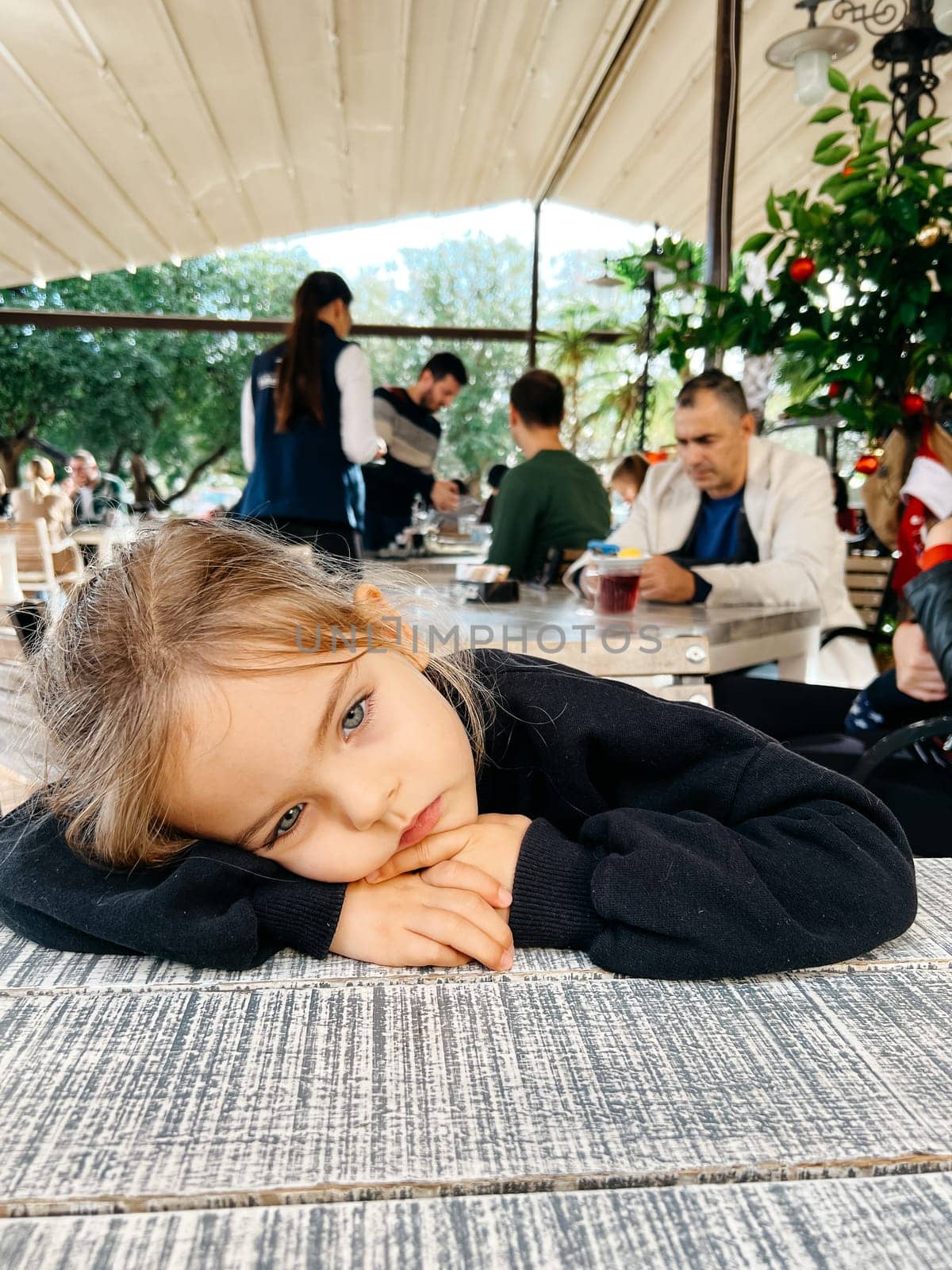Little girl sits with her head on her hands at a table in a restaurant. High quality photo