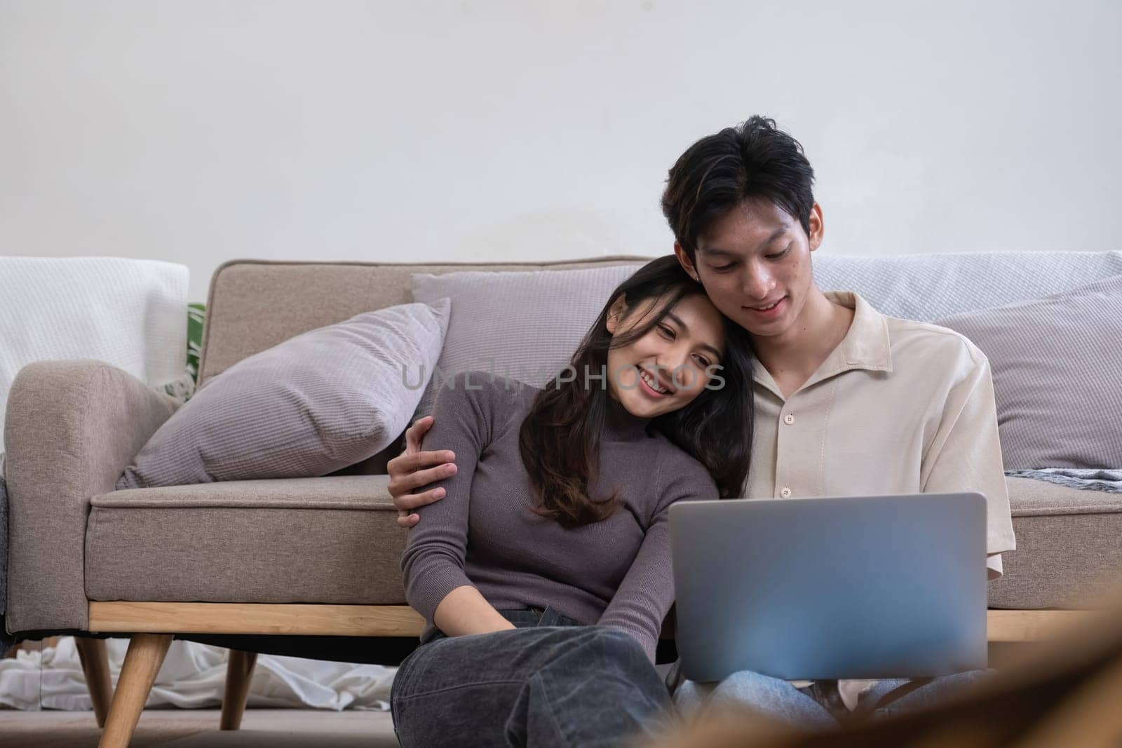 Young Asian couple in love Sitting happily together looking at laptop and relaxing in the living room. Couple making romantic love in the living room.