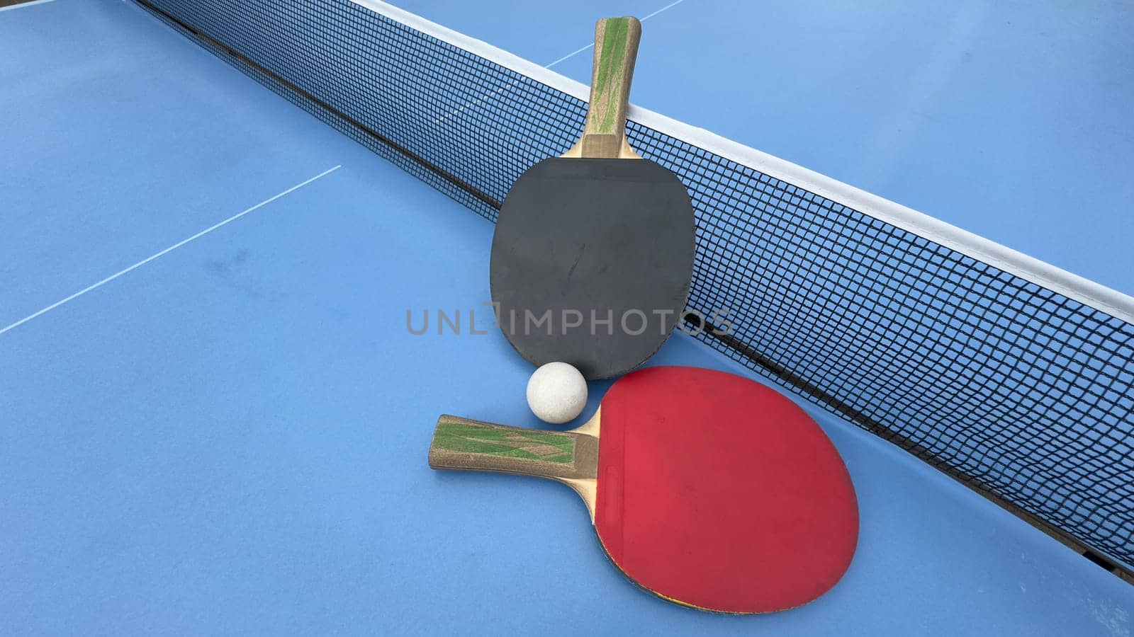 Two table tennis rackets and balls on a blue table with net. High quality photo