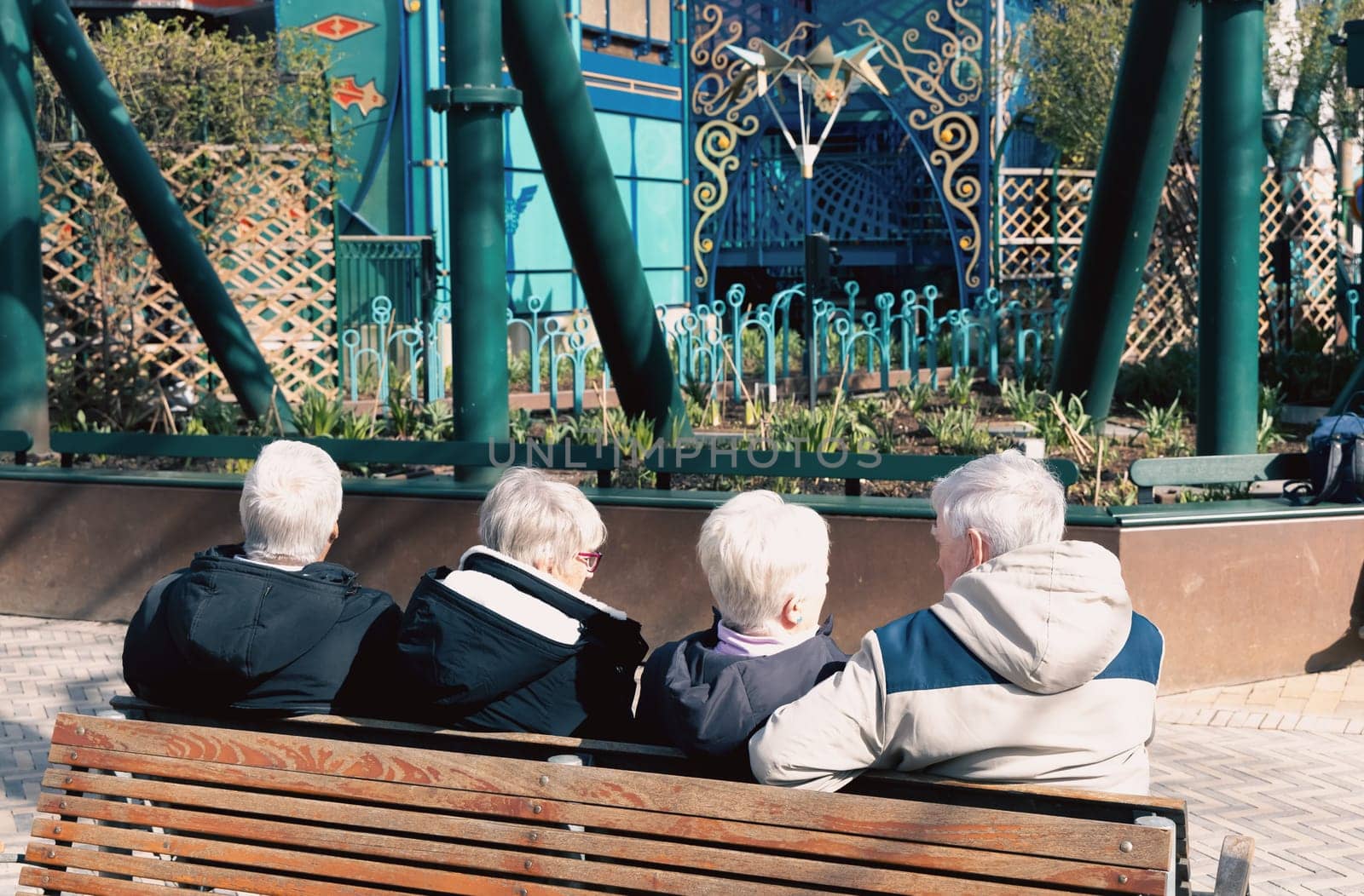 Four elderly people with gray hair are sitting and relaxing on a bench in the park. Retirement lifestyle.