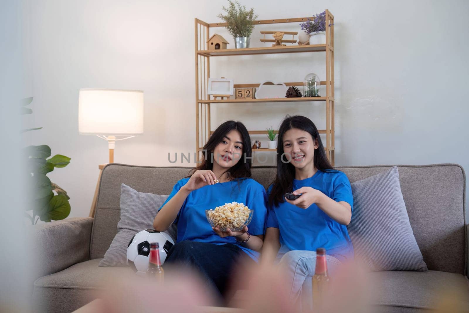 Friends watching a football game at home. Two women enjoying a sports match on TV with popcorn and snacks by nateemee
