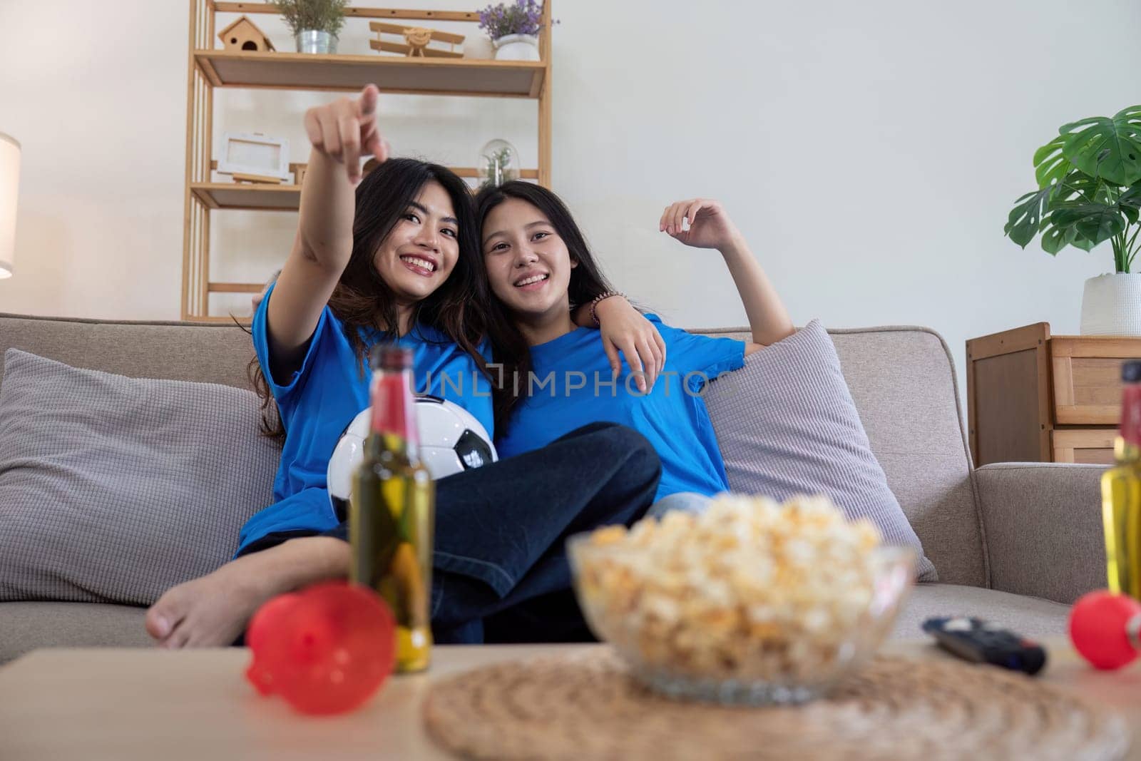Friends cheering while watching a football game at home. Two women enjoying a sports match on TV with popcorn and drinks by nateemee