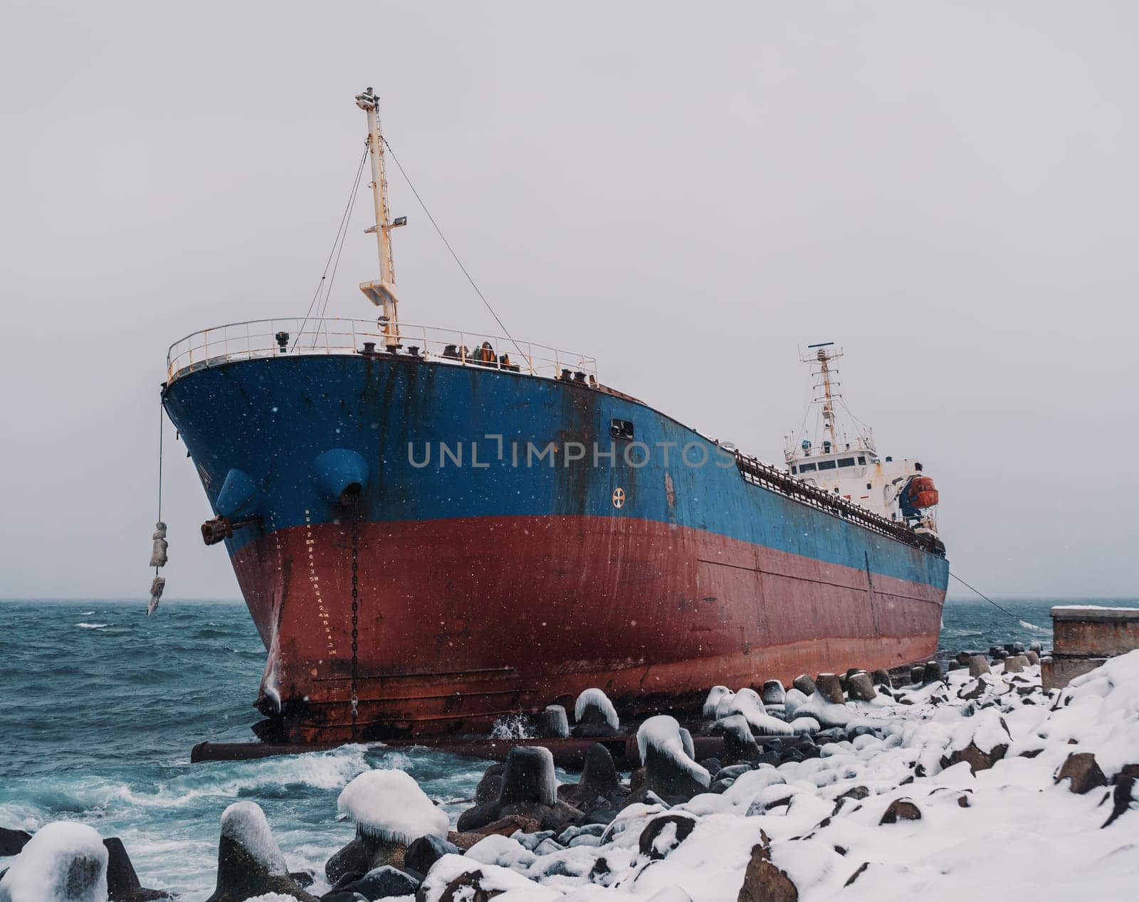 Cargo ship strands aground on a rocky shore after a storm, surrounded by snow and heavy waves. by Busker