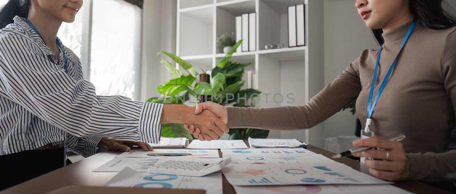 Asian women shaking hands in a modern office. Concept of business agreement, partnership, and success by nateemee