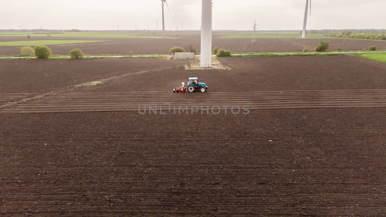 Seeds to sow. A tractor sows seeds against a background of meadows with wind turbines at sunset