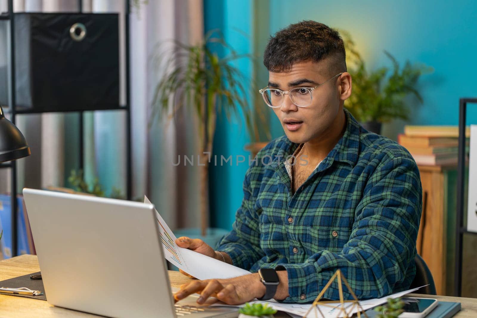 Indian freelancer man accountant working with financial graph documents calculate taxes for charts and reports at home office desk. Businessman guy working on laptop computer planning expenses budget