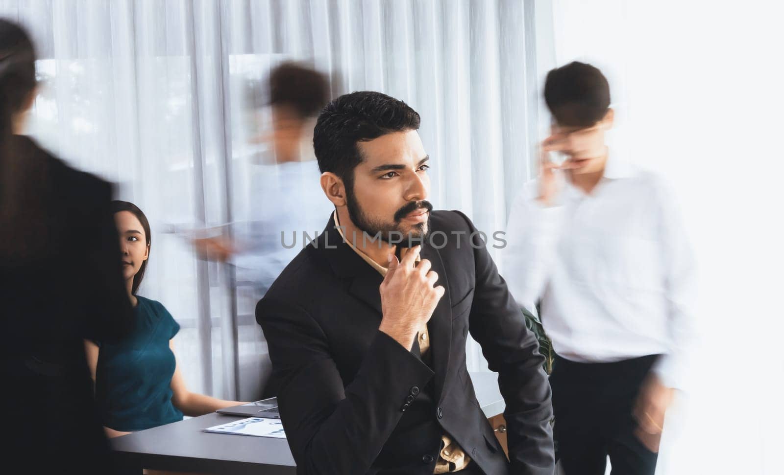 Businessman portrait poses confidently with diverse coworkers in busy meeting room in motion blurred background. Multicultural team works together for business success. Concord