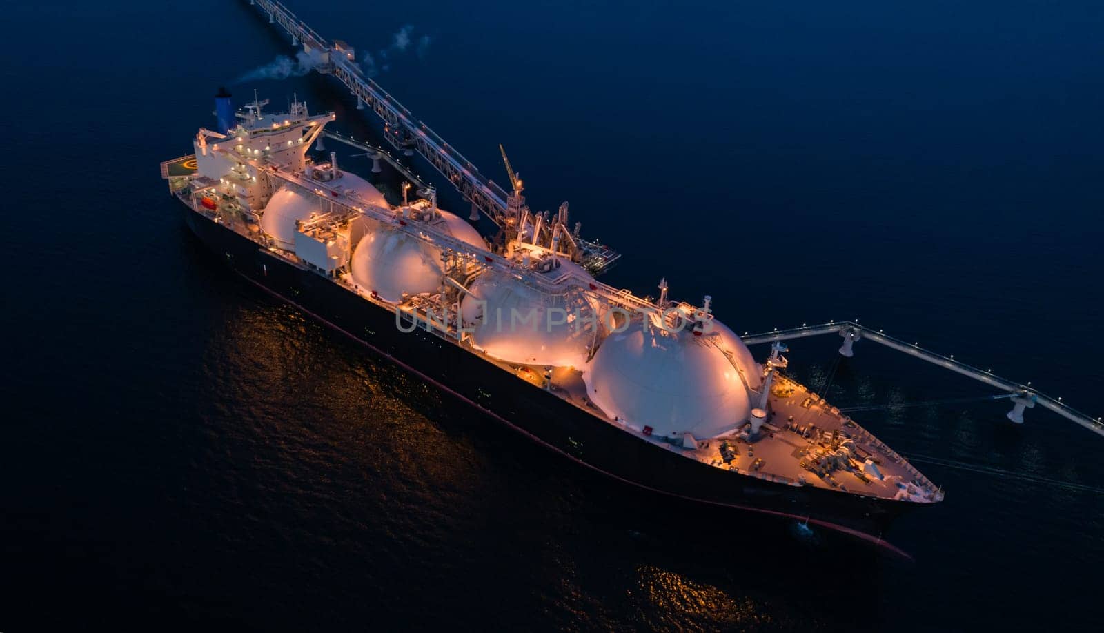 Aerial of Liquified Natural Gas LNG carrier moored to a small gas terminal at night. Fuel crisis. Sanctions. Top down shot.