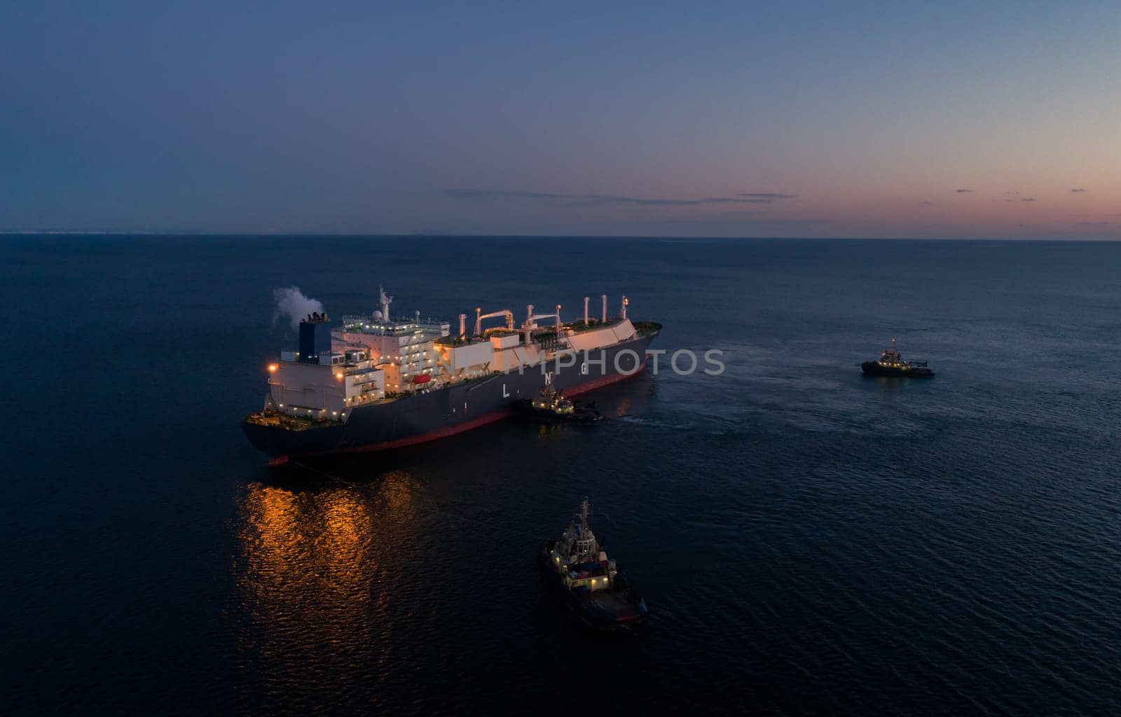 A large LNG tanker docks at an industrial port terminal for cargo operations at dusk by Busker