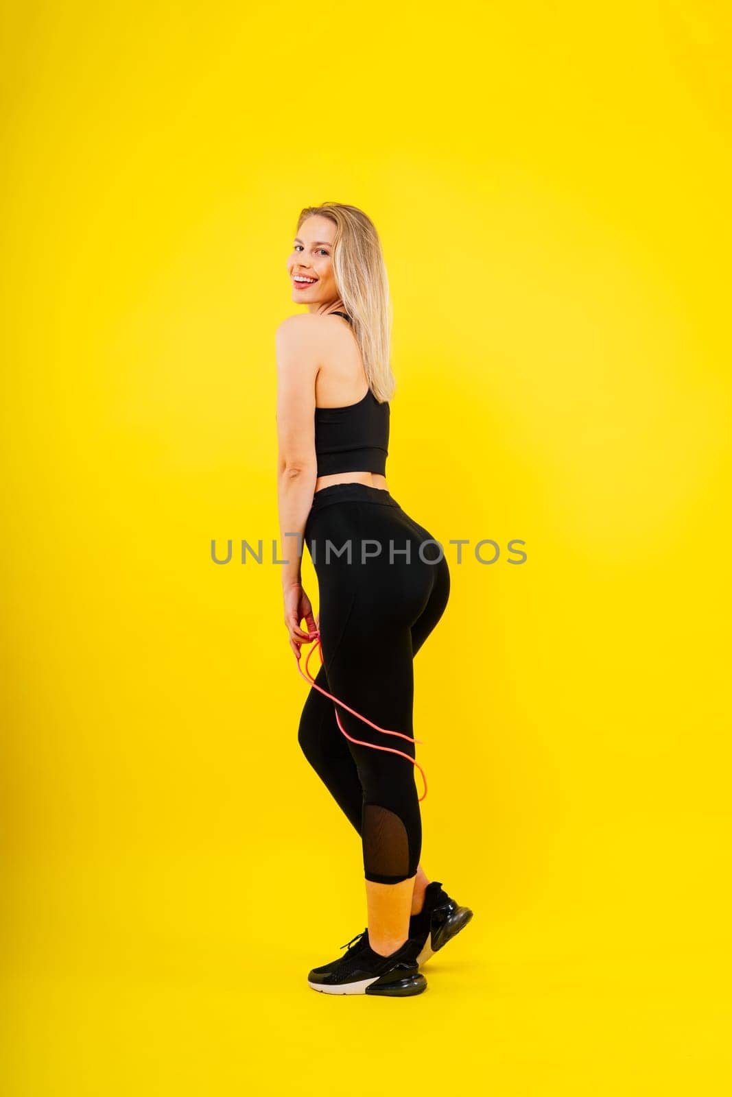 Blond woman with jump rope in studio, yellow red and dark background by Zelenin