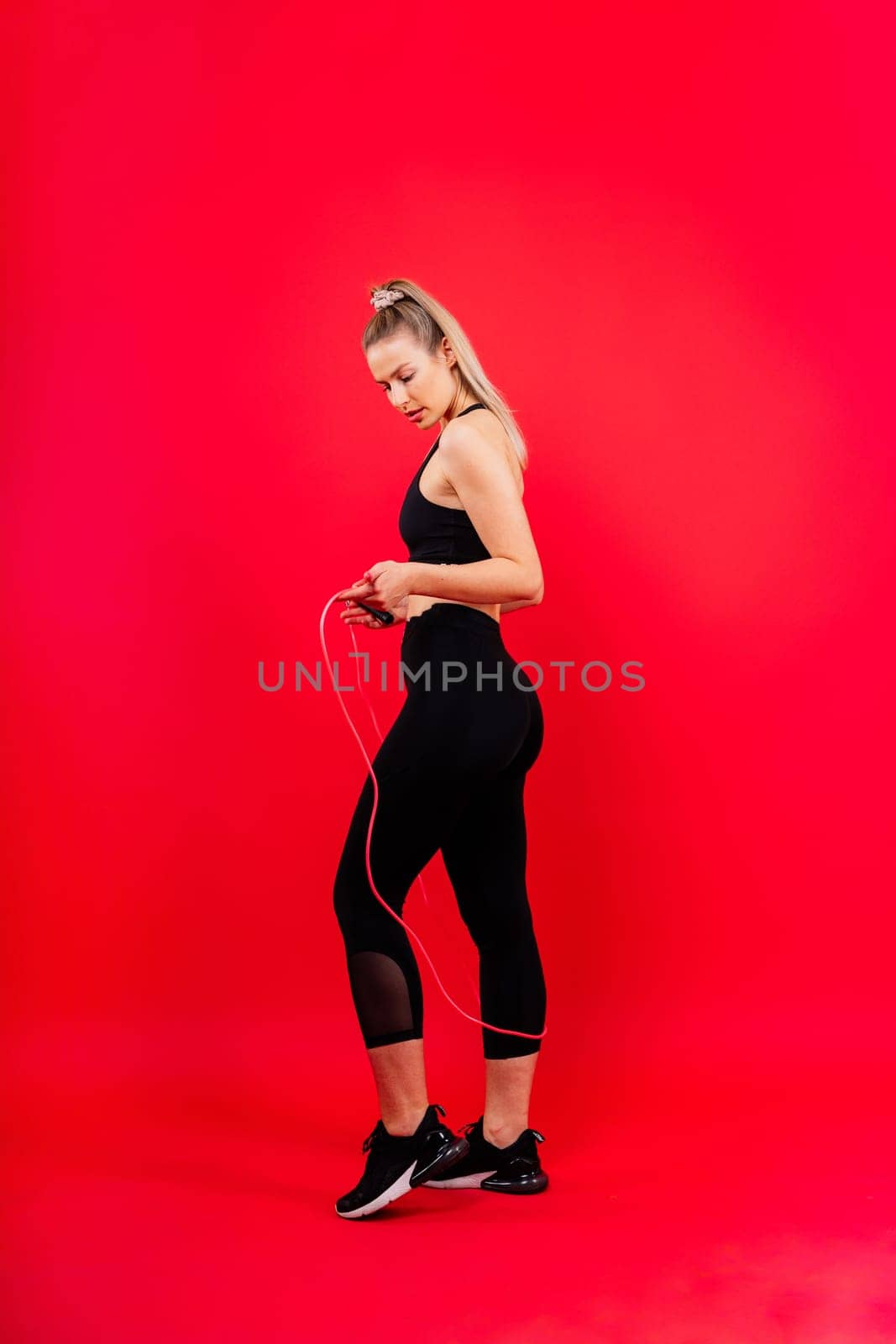Blond woman with jump rope in a studio, yellow red and dark background