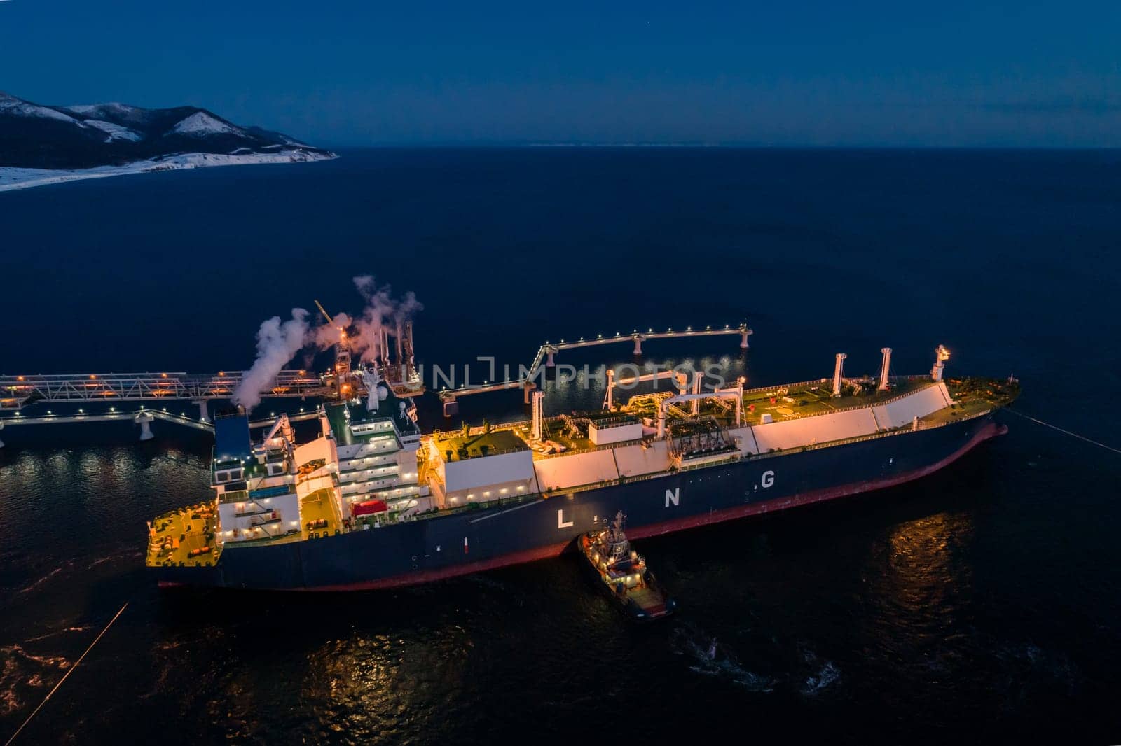 A large LNG tanker docks at an industrial port terminal for cargo operations at dusk