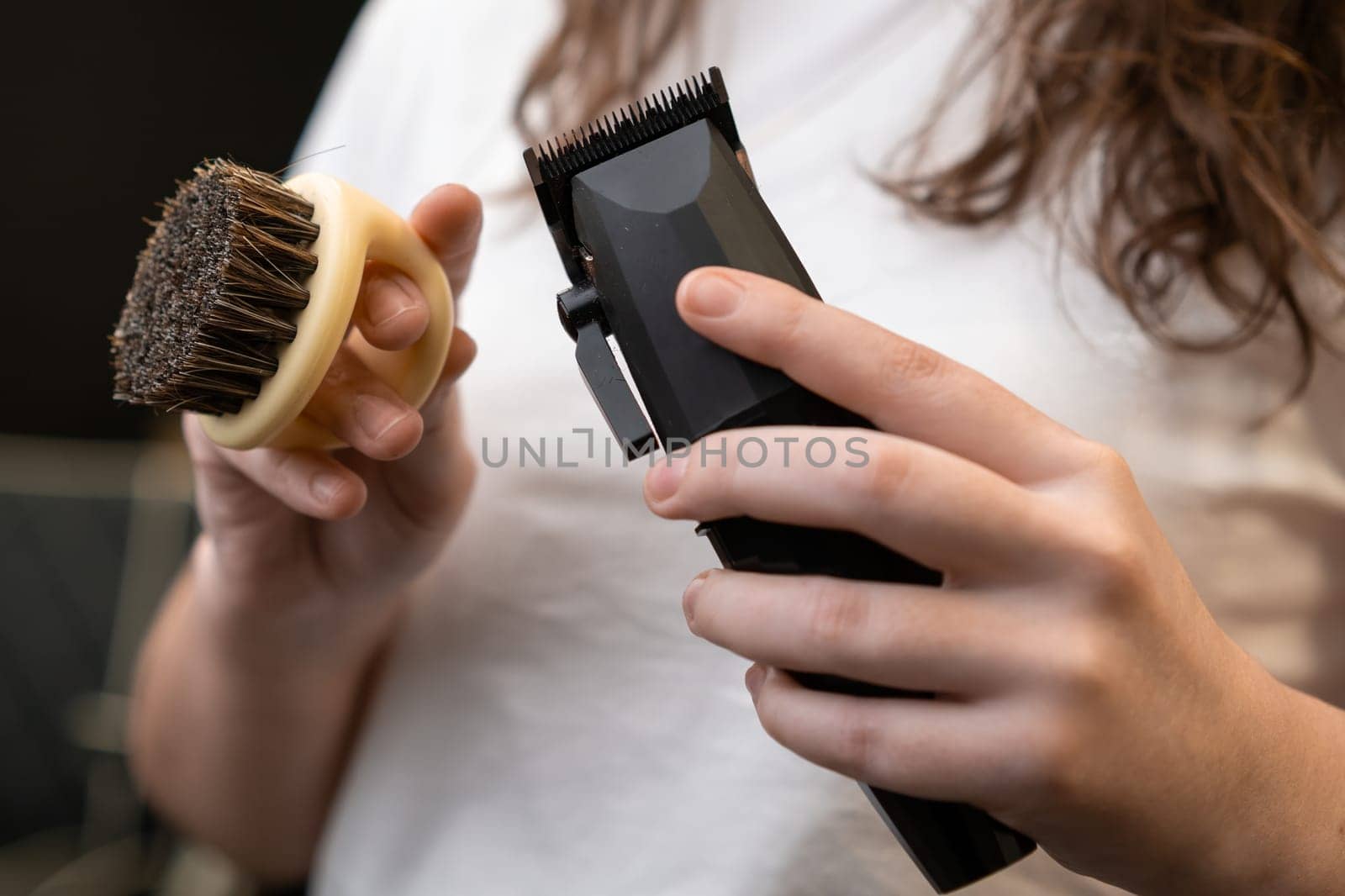 Woman barber holding trimmer and brush in her hands in barbershop.