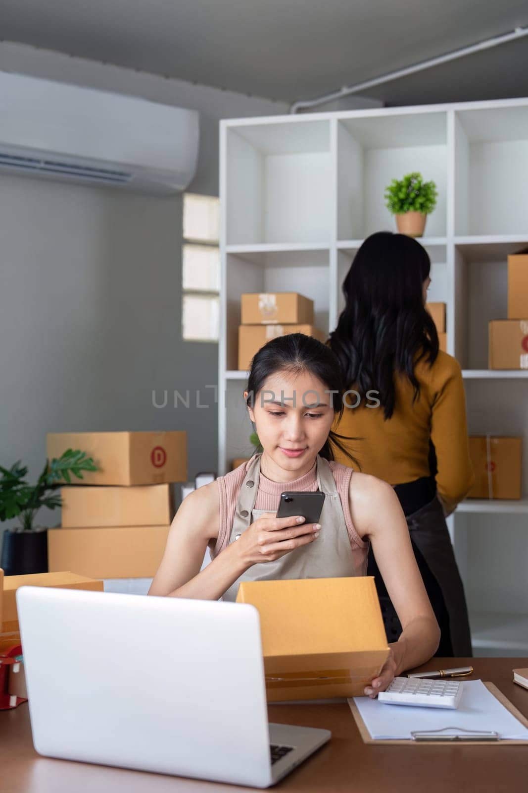 Entrepreneur managing online business from home office. ecommerce owner preparing packages for shipment and checking orders on a smartphone. by nateemee