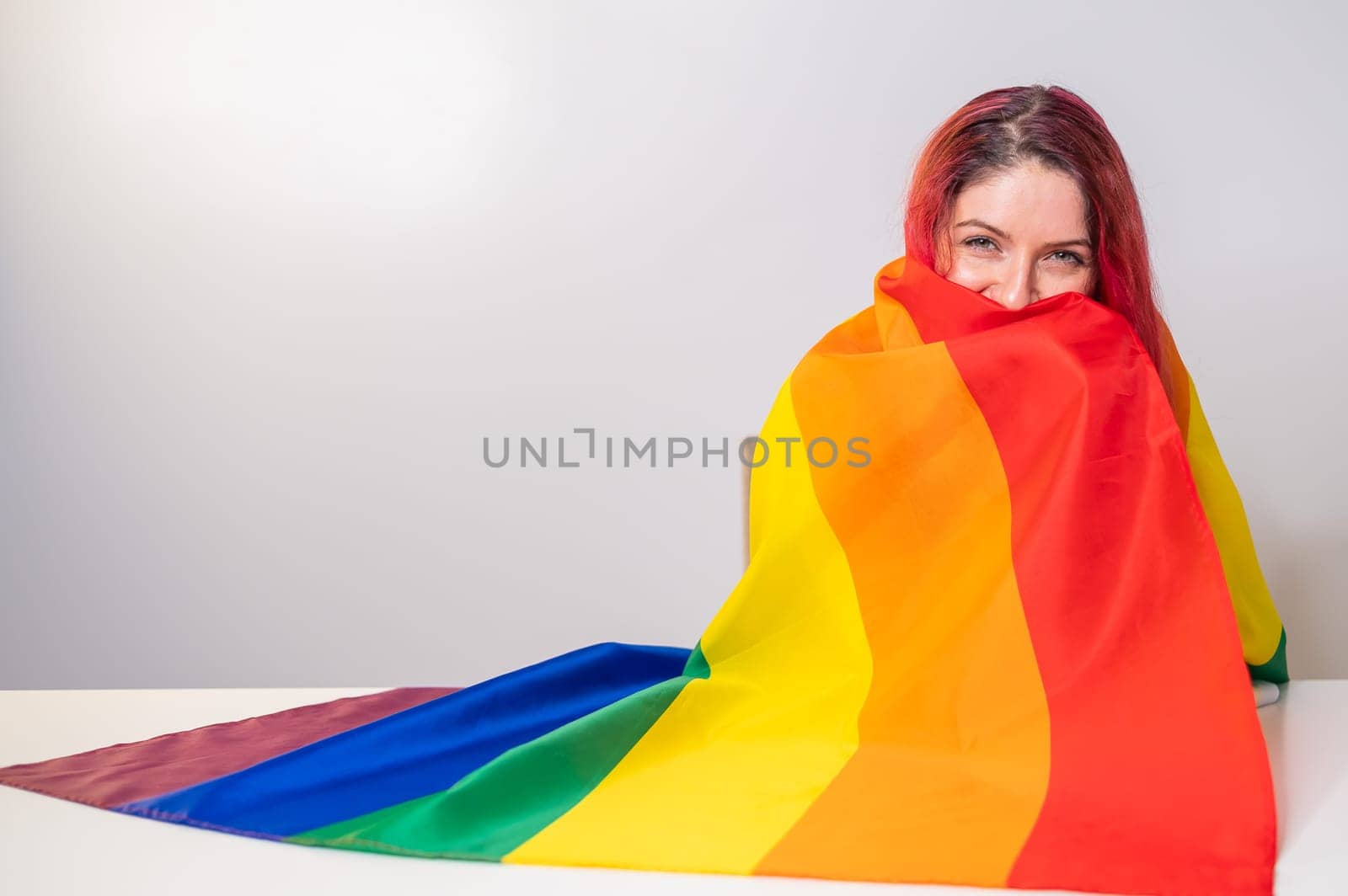 Young red-haired woman taking cover with lgbt flag on white background by mrwed54
