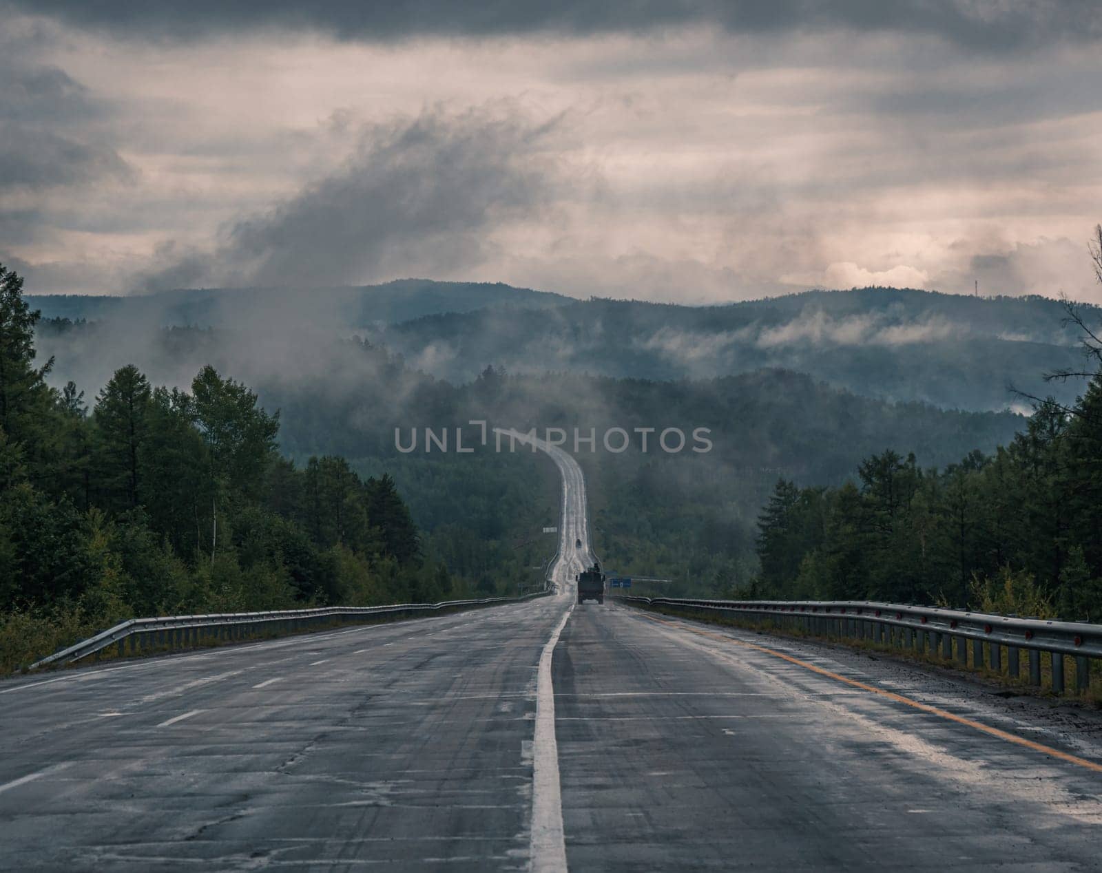 Straight empty highway stretching toward distant forest on a cloudy day by Busker