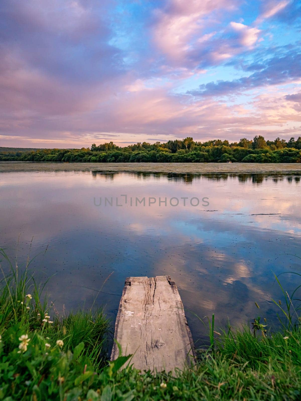 Beautiful pink sunset over calm lake at countryside evening. Tranquil lake with a wooden dock in the foreground. by Busker