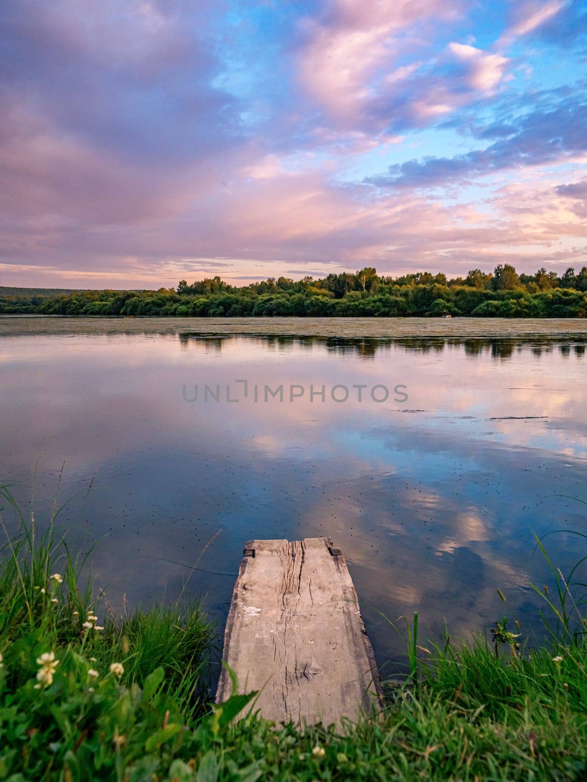 A serene countryside scene during sunset, showcasing a tranquil lake with a wooden dock in the foreground.