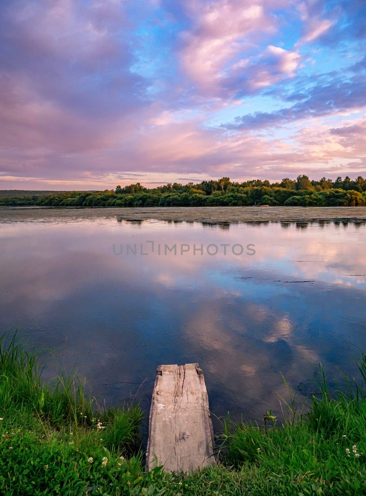 A serene countryside scene during sunset, showcasing a tranquil lake with a wooden dock in the foreground.