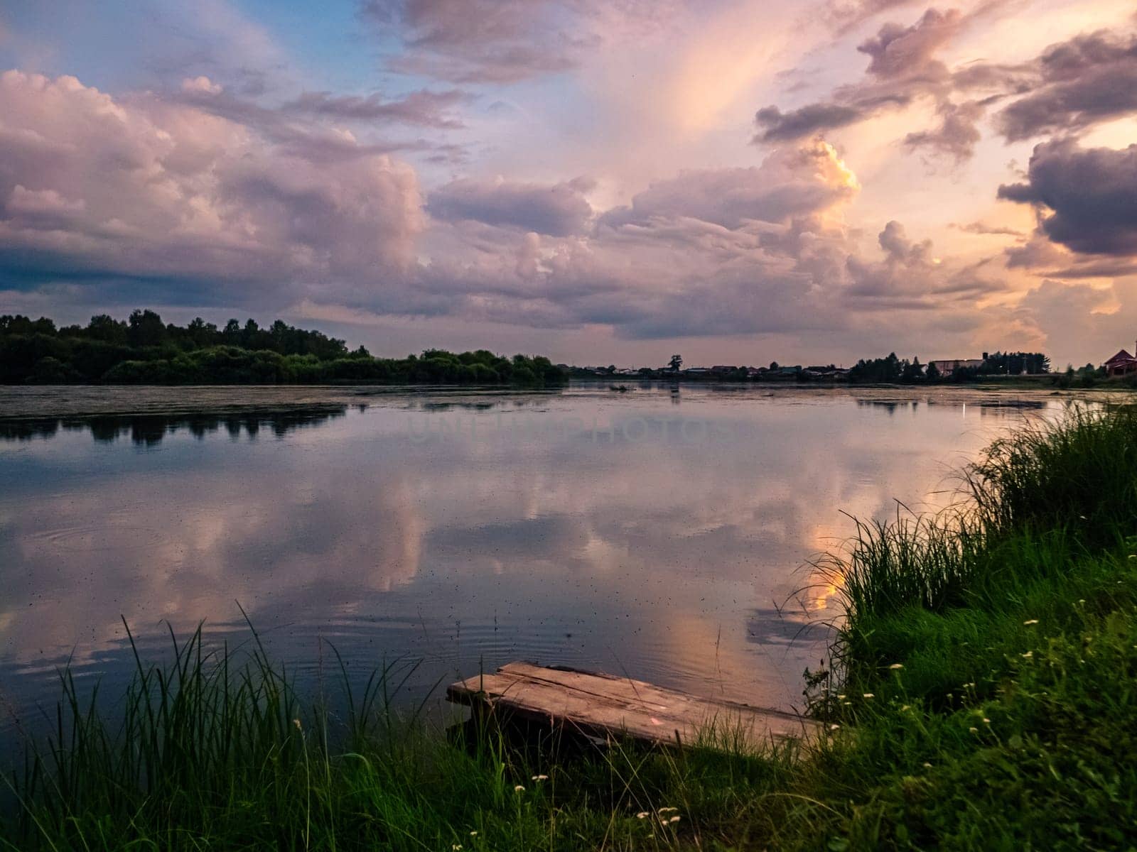 A serene countryside scene during sunset, showcasing a tranquil lake with a wooden dock in the foreground.