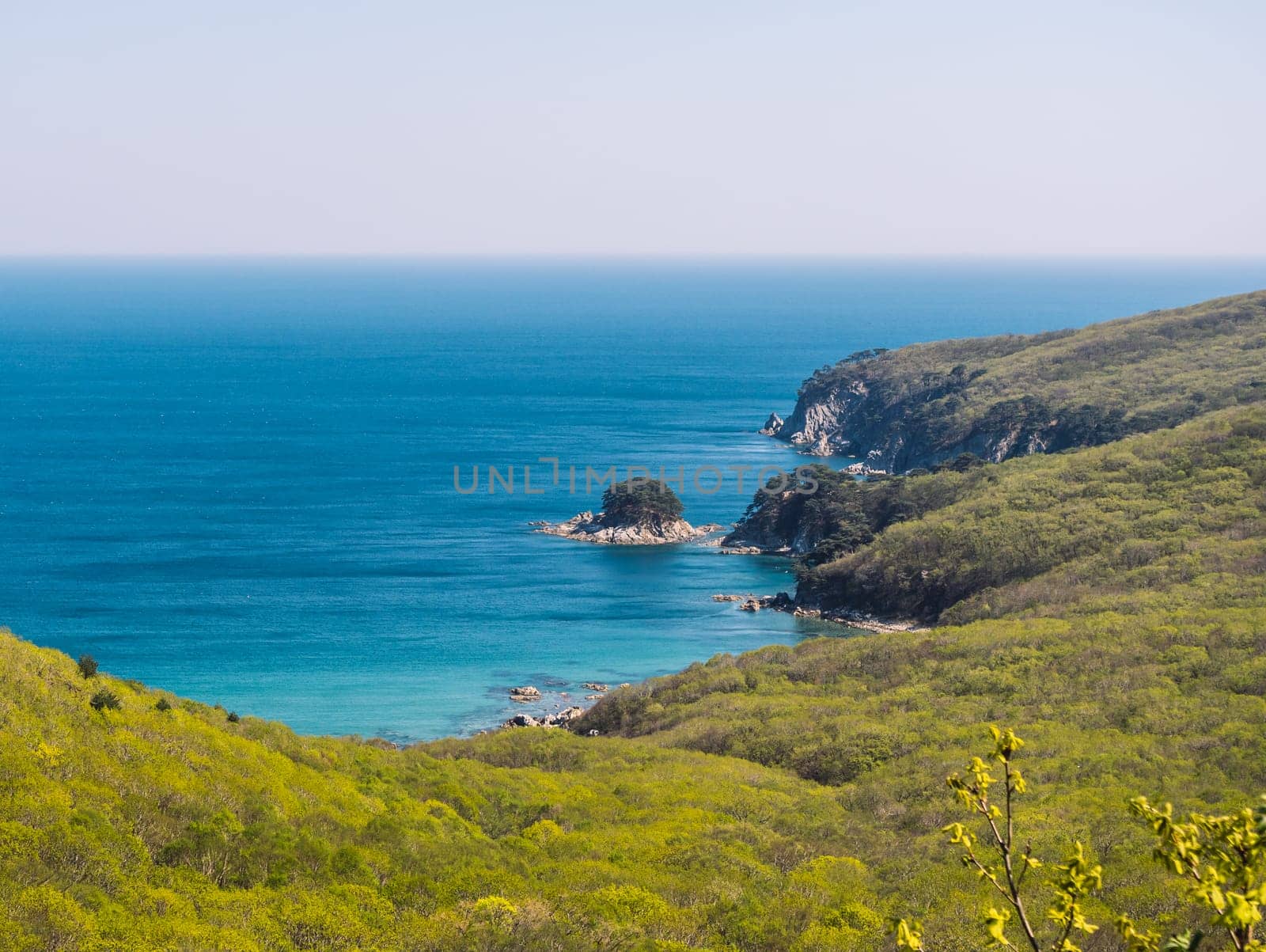 Serene view of rugged coastline and clear blue sea on a sunny day by Busker