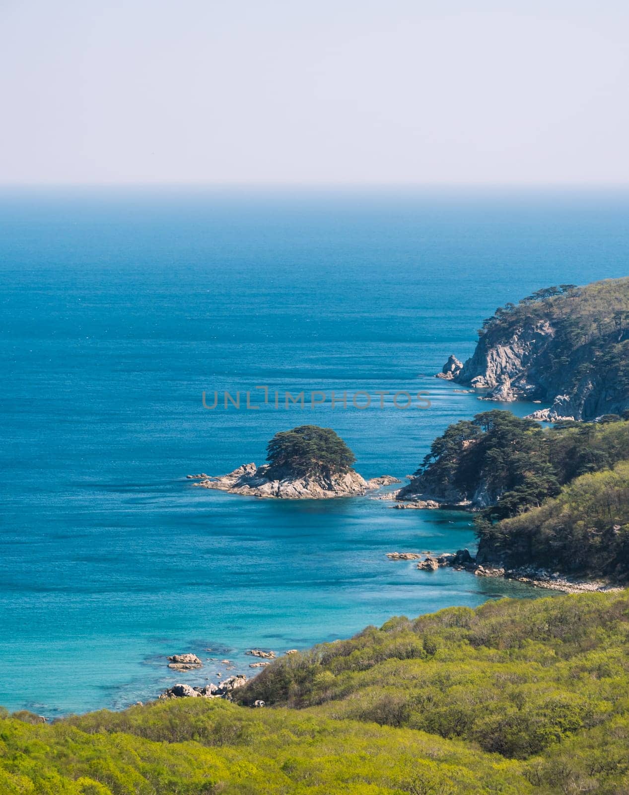 Serene view of rugged coastline and clear blue sea on a sunny day by Busker