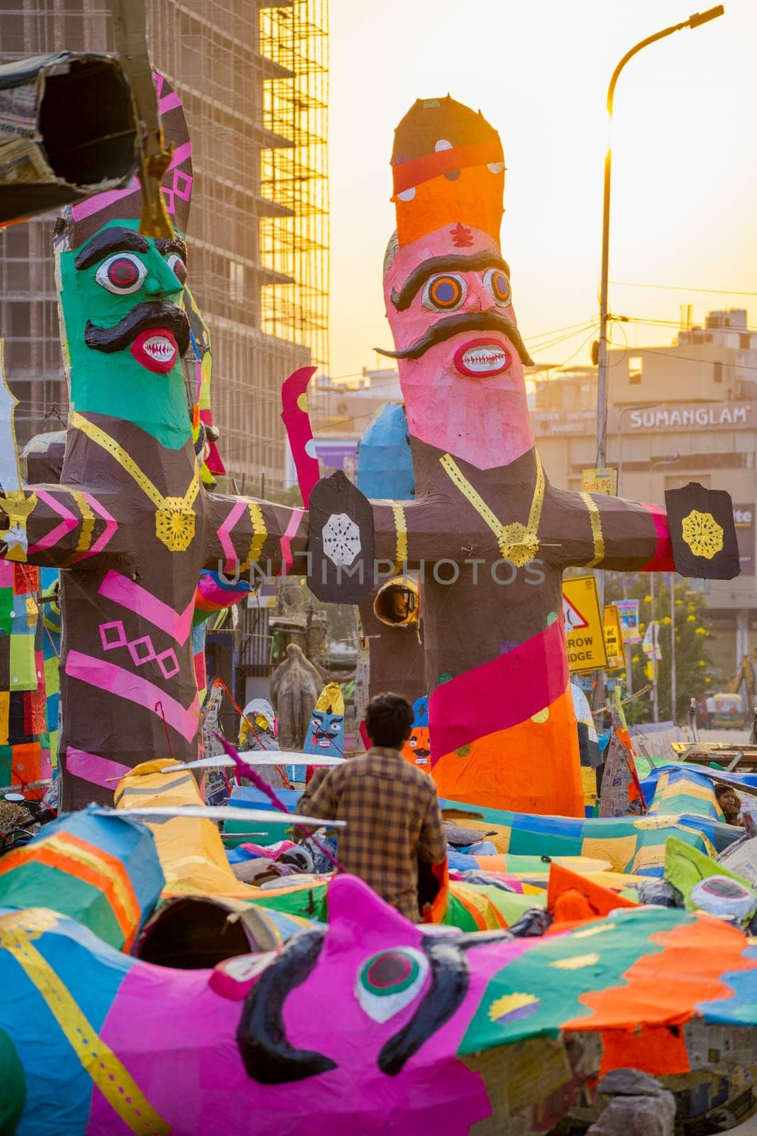 man standing looking at the colorful paper effigies of ravan made by him ready for sale on the side of a busy road
