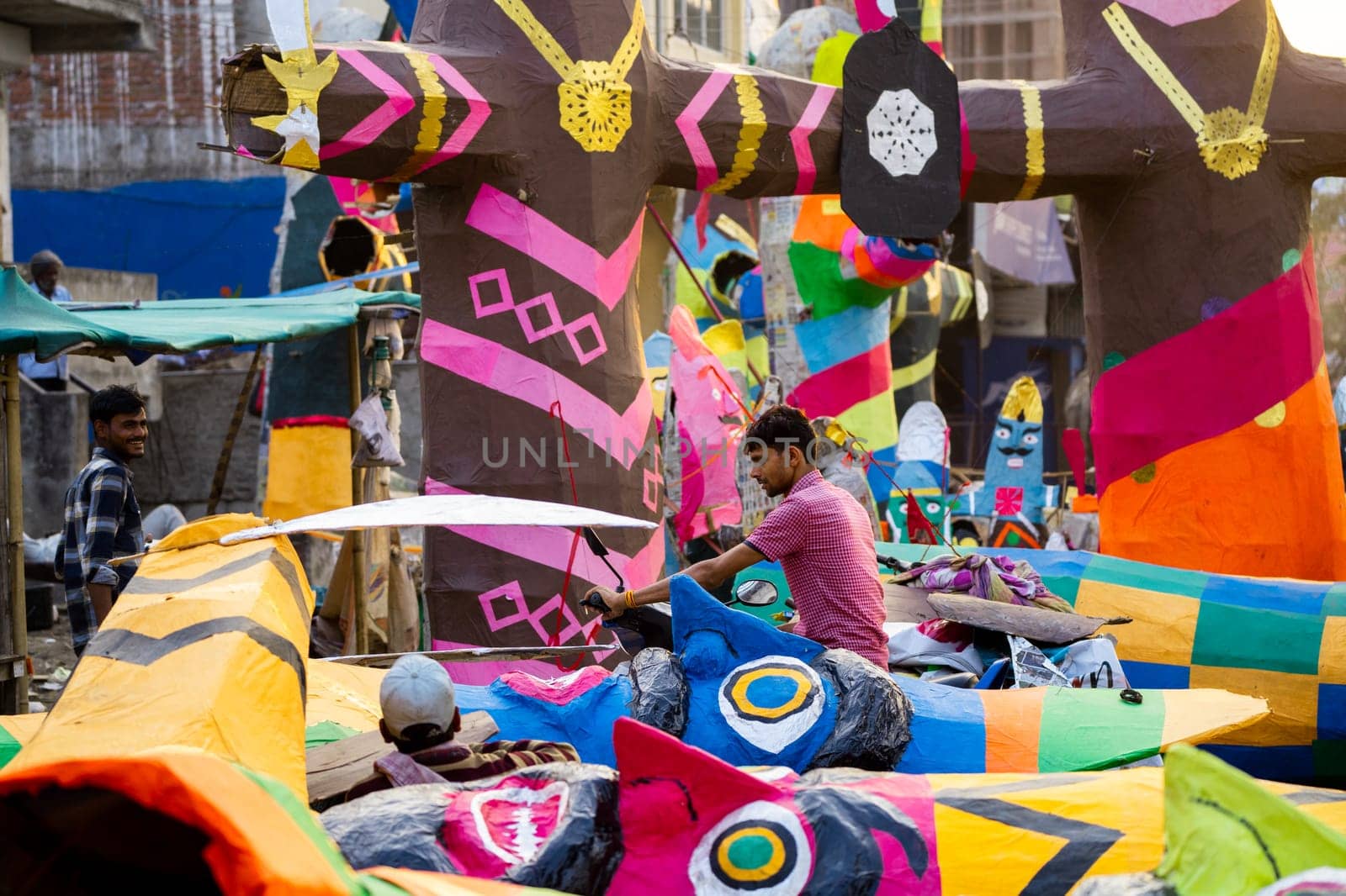 man standing in the middle of huge colorful effigies of ravan choosing one to buy on dussehra celebrations by Shalinimathur