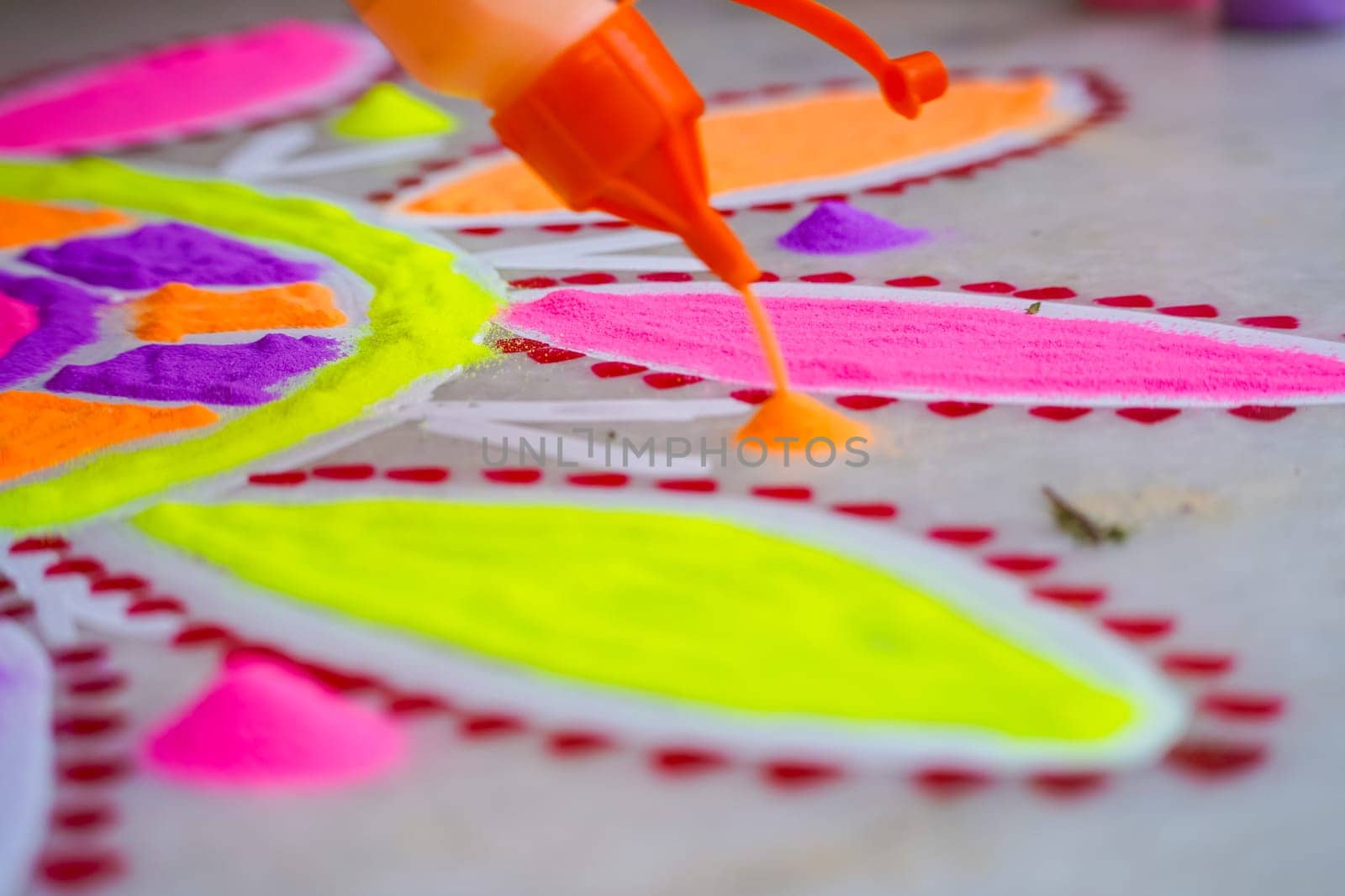 Woman using a bottle of pour a mound of orange color onto the ground to make a colorful rangoli a traditional art made on floors during festivals of diwali, dussera, onam in hindu culture
