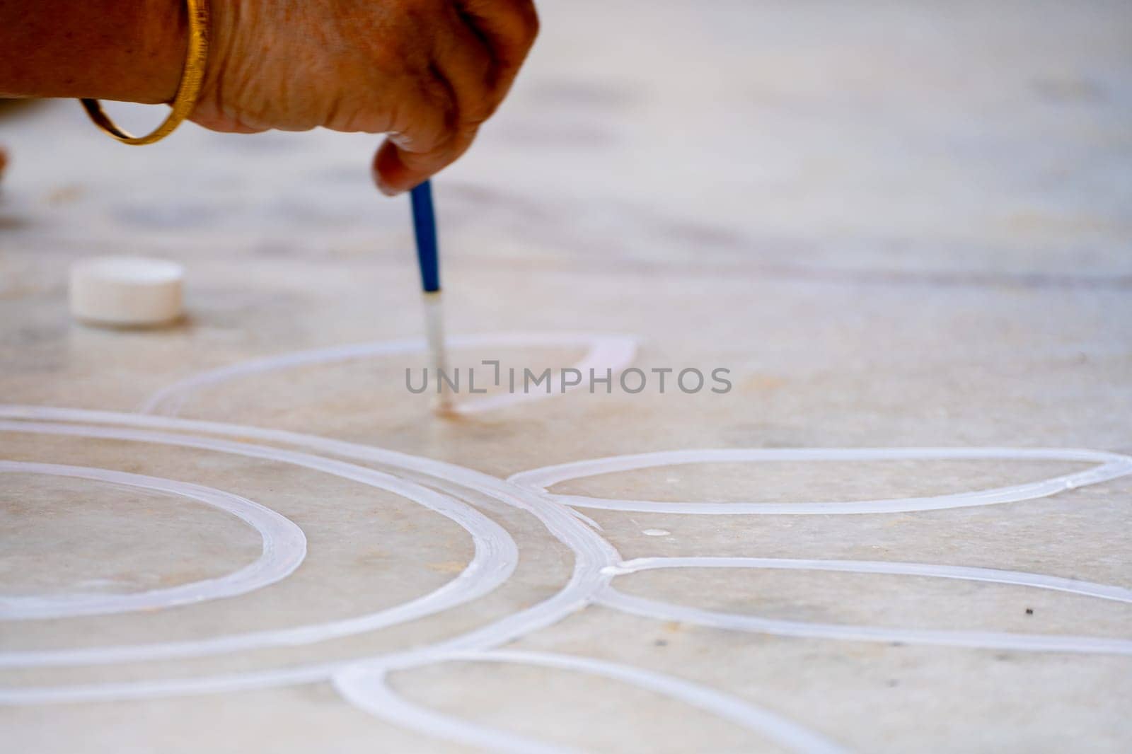 Woman using a paintbrush to make designs on ground for a rangoli a traditional art made on floors during festivals of diwali, dussera, onam in hindu culture by Shalinimathur