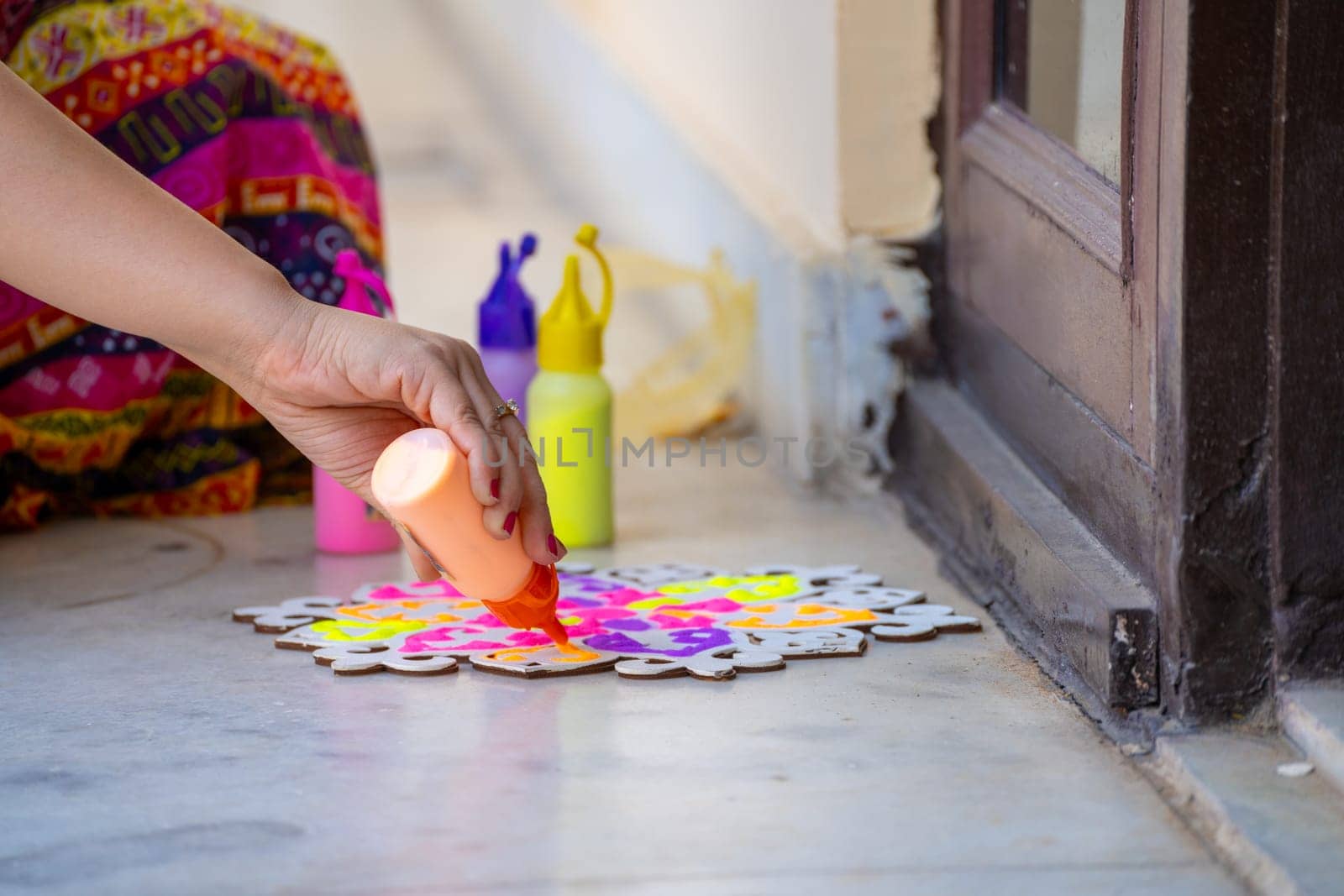 Indian woman in traditional indian clothing using bottles of color powder to make rangoli a traditional art made on floors during festivals of diwali, dussera, onam in hindu culture by Shalinimathur