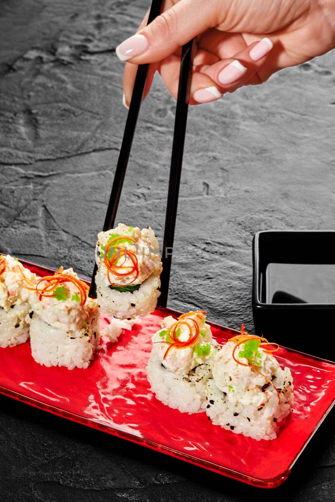 Female hand using chopsticks to pick up sushi roll with creamy seafood toppings by nazarovsergey