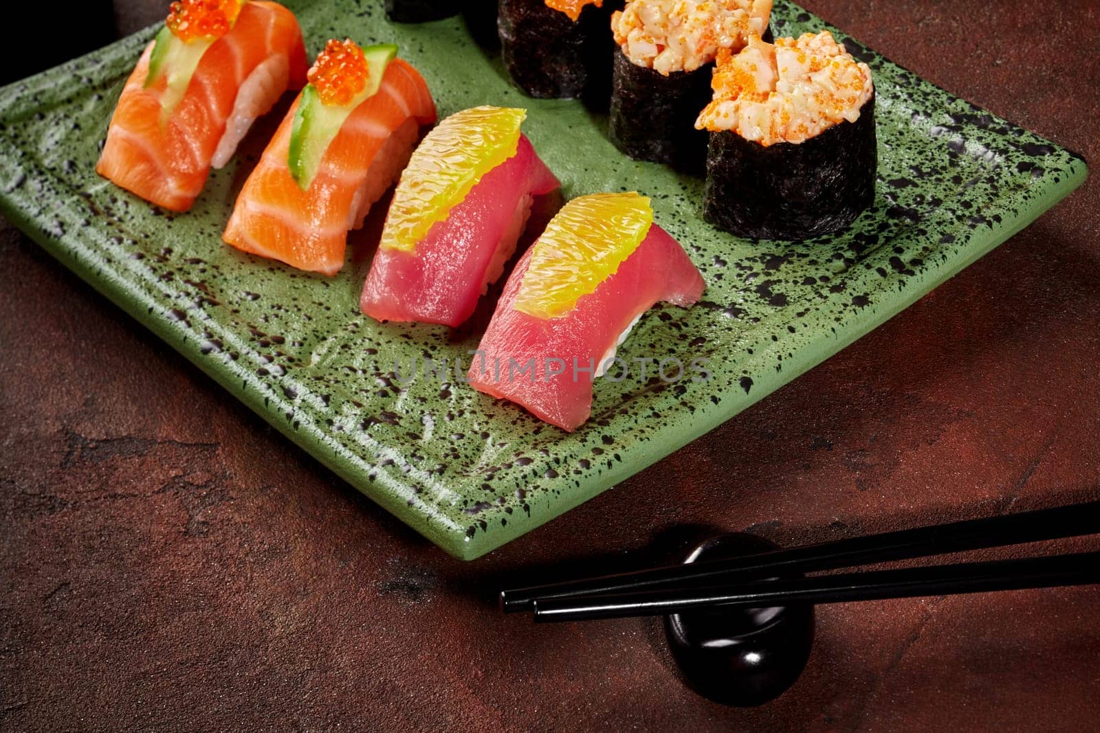 Vibrant sushi set of hand-tossed nigiri with tuna and salmon garnished with orange, cucumber and caviar, and gunkan maki with creamy fish and roe filling on mottled green ceramic plate with chopsticks