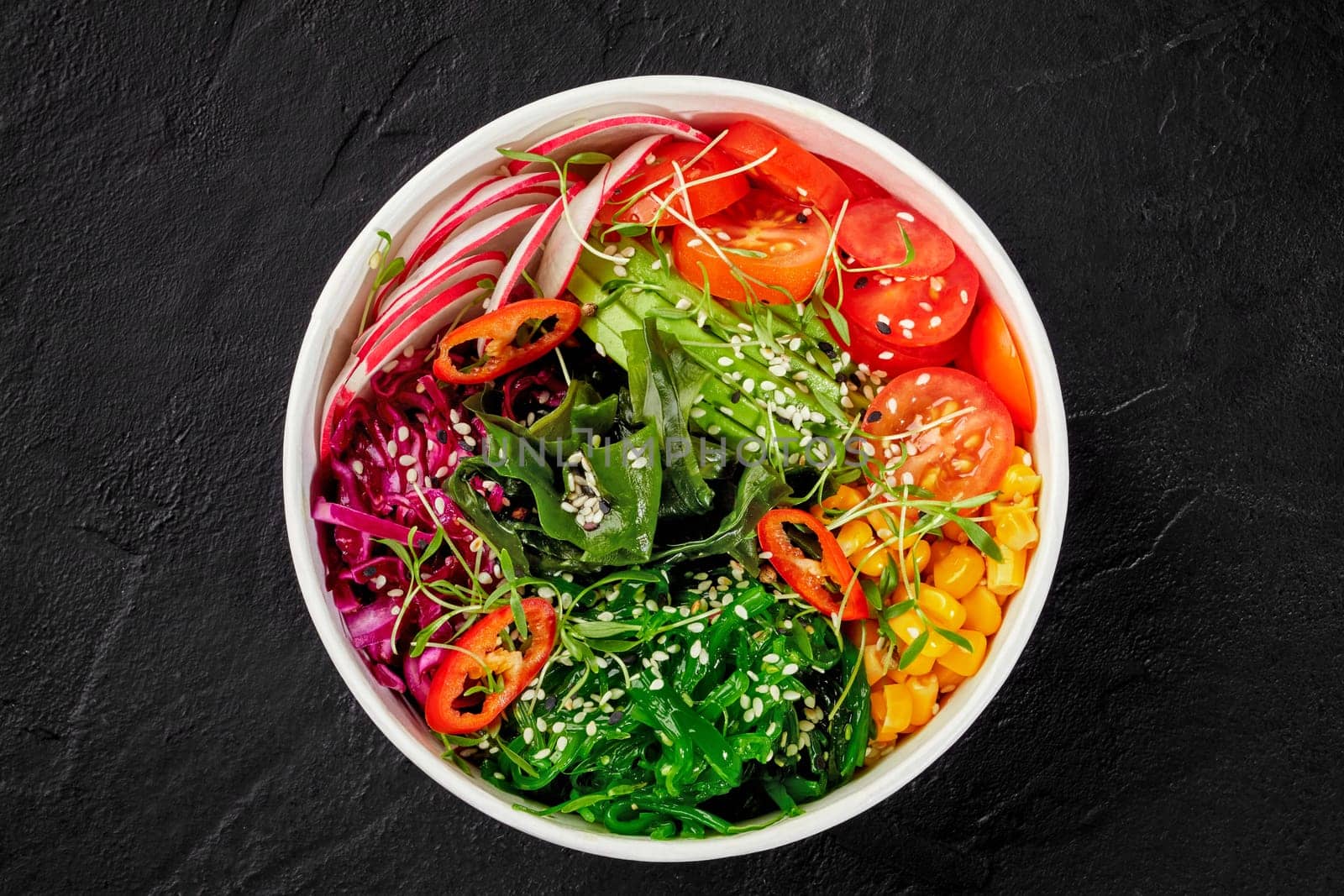 Bright and colorful vegan poke bowl, packed with variety of fresh vegetables, seaweed, and sprinkled with white sesame seeds, served on dark slate background. Healthy snack. Delivery food concept