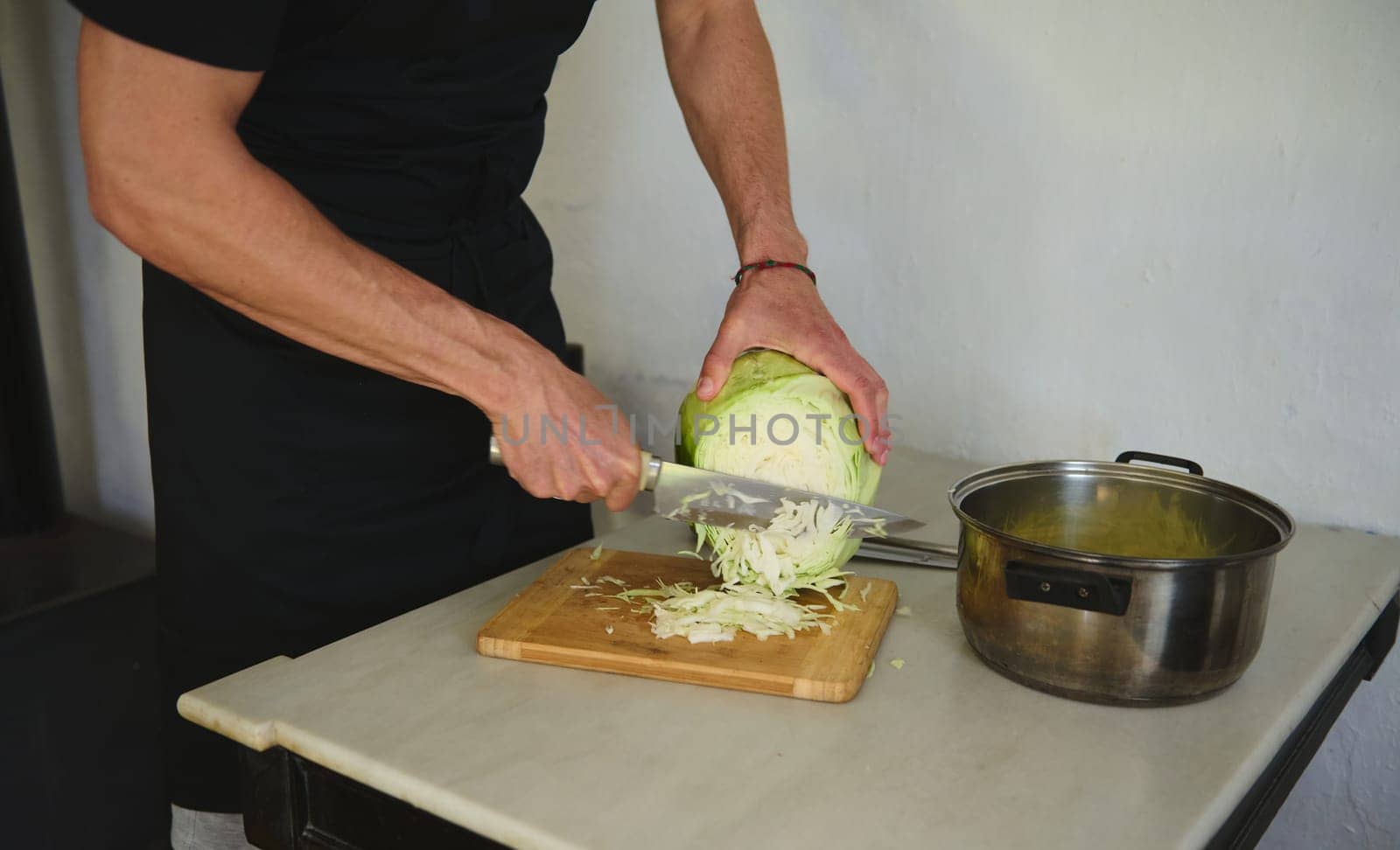 Close-up male chef chopping raw fresh cabbage on a wooden board in rustic home kitchen. Food concept