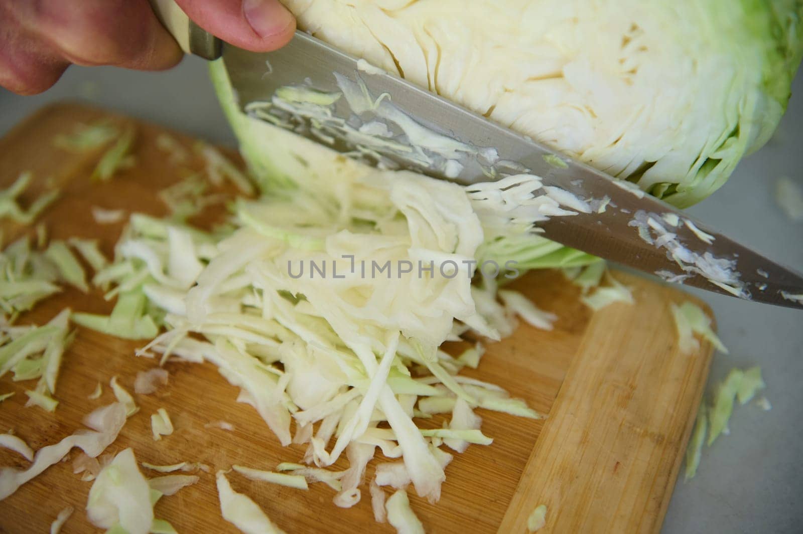 Close-up of a chef man using kitchen knife, chopping slicing cutting raw fresh cabbage on a wooden board, preparing raw organic vegan salad