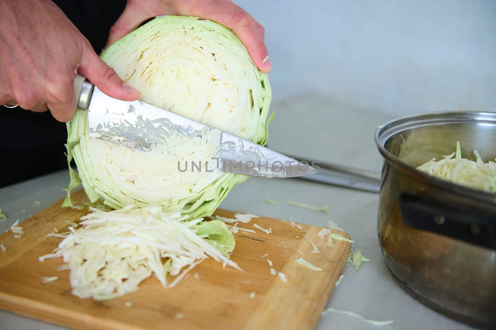 Close-up chef man using kitchen knife, slicing cutting raw fresh cabbage on a wooden board, preparing raw organic vegan salad