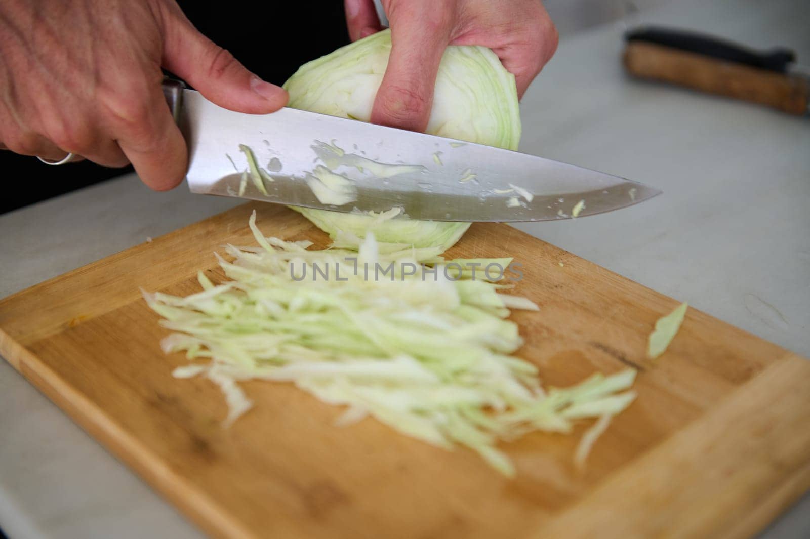 Close-up view of a man chopping raw fresh cabbage on a wooden board