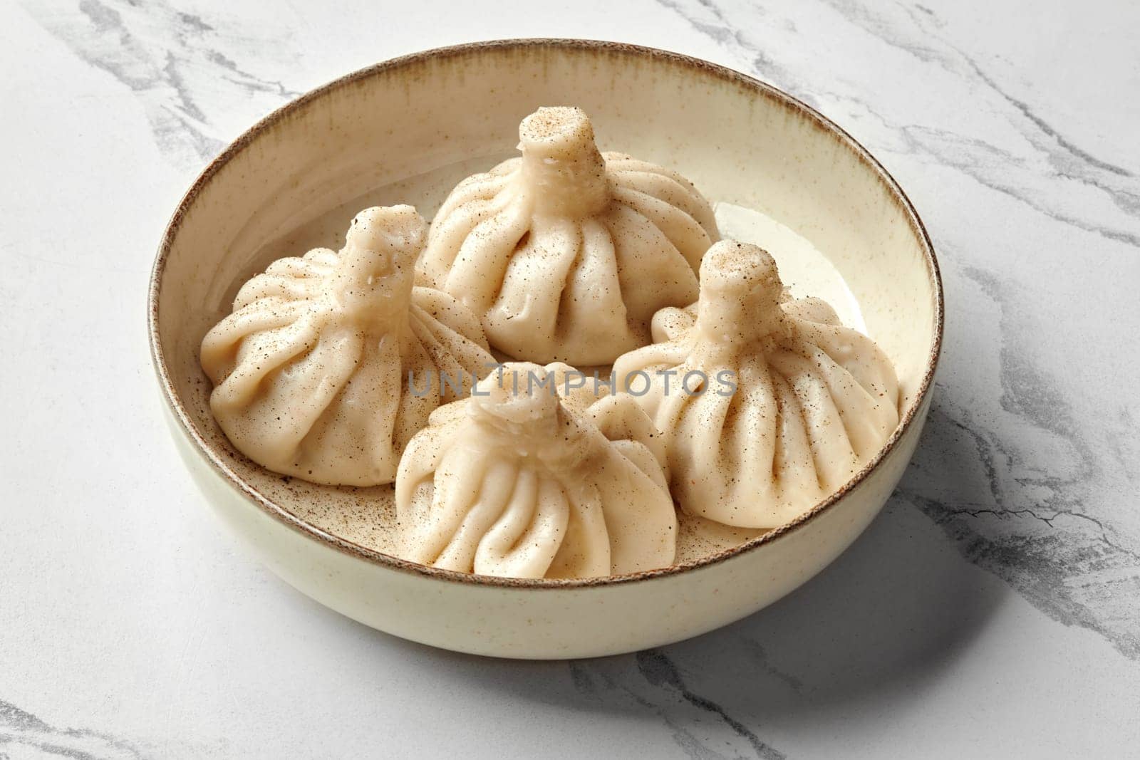 Traditional juicy Georgian khinkali dumplings stuffed with spiced minced meat sprinkled with black pepper, presented on speckled ceramic plate against marble surface