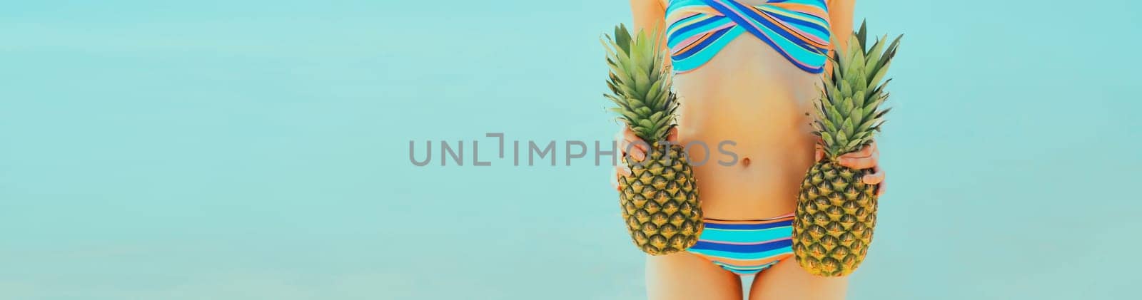 Summer vacation, close up beautiful young woman in bikini swimsuit with two pineapples on the beach on sea coast background, advertising banner copy space