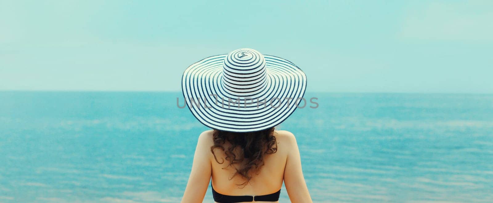 Summer vacation, rear view of beautiful relaxed young woman in hat on the beach on sea background by Rohappy