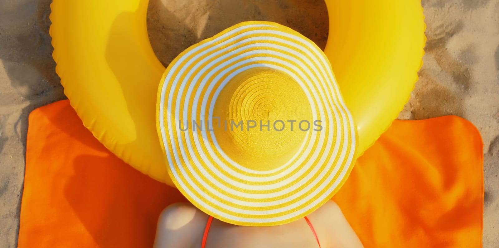 Summer vacation, happy relaxing young woman with straw hat covering her face lying on sand on the beach with swimming inflatable ring