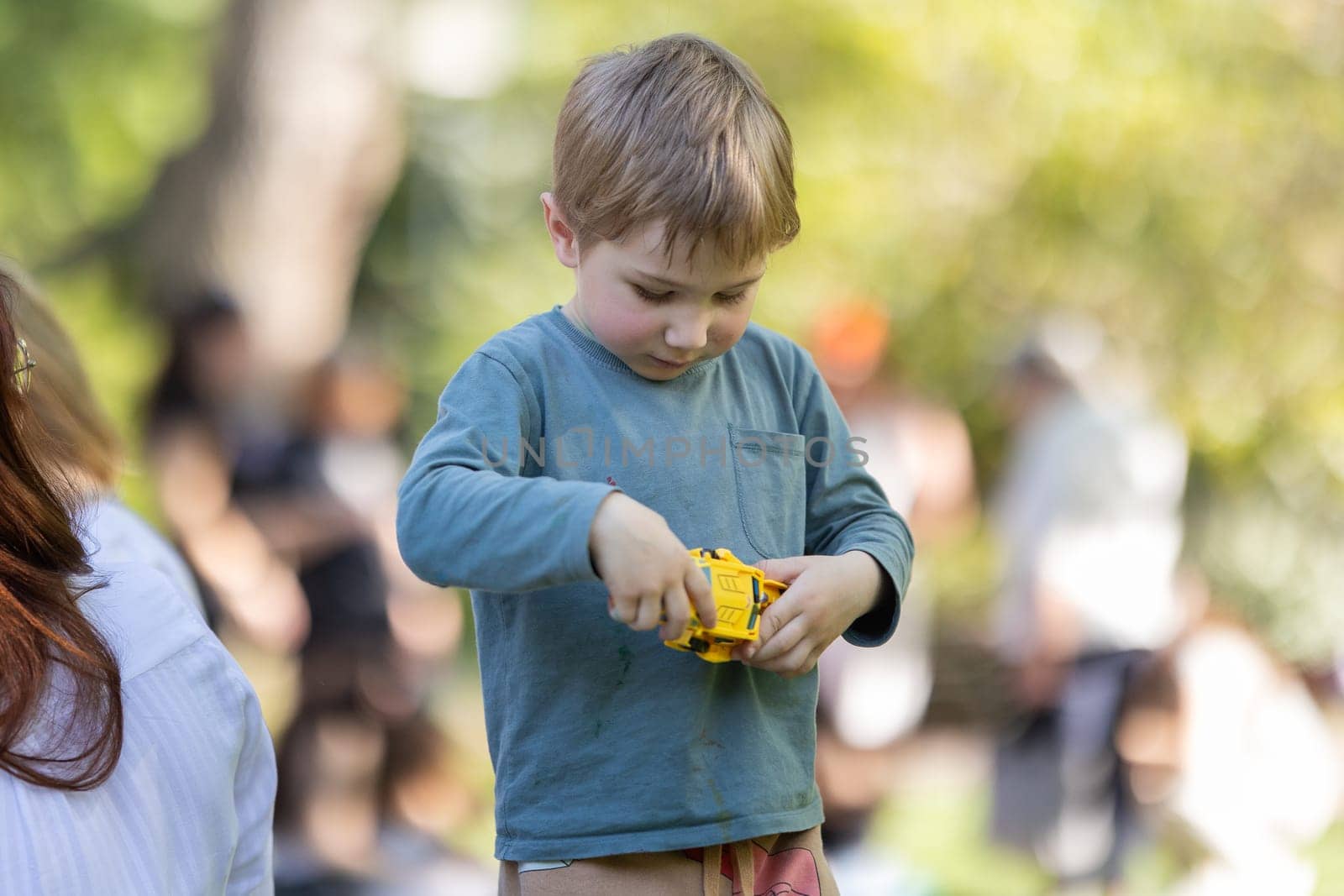A boy is playing with a toy car. He is holding it in his hands and looking at it