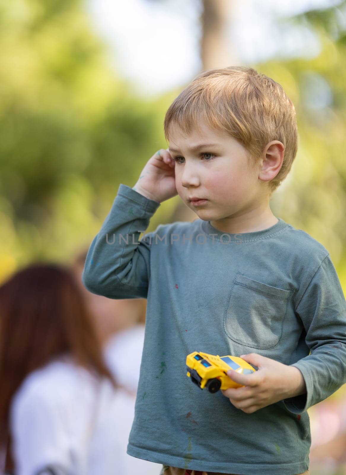 A young boy is holding a toy car and talking on a cell phone. He is wearing a green shirt and has a pocket on his shirt